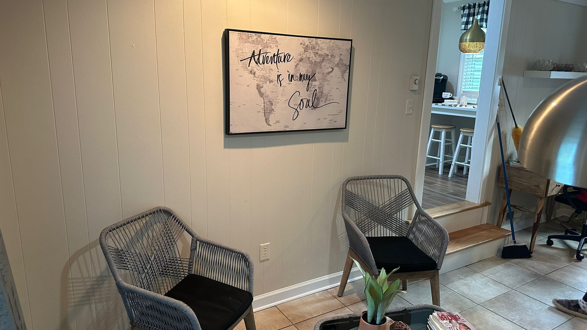 A room with two wicker chairs, a world map artwork, a coffee machine, and a small table with a plant.