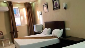 A hotel room with two beds, a desk, a chair, and a window with curtains. - Hôtel kassar  (Oran)