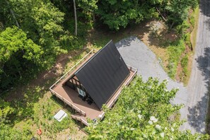Luchtbeeld van een chalet met schuin dak, omringd door weelderige begroeiing en een grindpad.