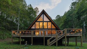 Une cabane dotée d’un toit triangulaire, de grandes fenêtres et d’une terrasse en bois avec un escalier menant à l’entrée principale.