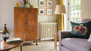 A living room with a wooden cabinet, a radiator, a lamp, a sofa with a floral pillow, and framed pictures on the wall. - The Room Rawsons in Levens (Kendal)