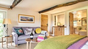 A cozy room with a sofa, a small table with a bottle and glasses, and a bed with a green blanket. - The Room Rawsons in Levens (Kendal)