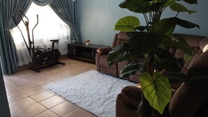 A living room with a sofa, a large plant, and an exercise bike. - Secure, Spacious & Fully Equipped – Your Ideal Townhouse Stay 4 (Pretoria)