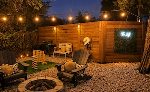 Un espacio al aire libre con sillas Adirondack, una fogata y una terraza de madera.