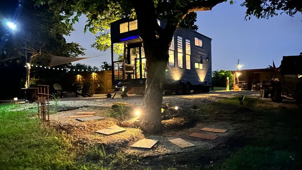 A treehouse with a glass facade, surrounded by a gravel area with stepping stones, and string lights. - Modern Tiny Home • Firepit • Near AT&T Stadium (Venus)