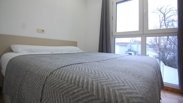 A bedroom with a bed, a window with curtains, and a view of the outside. - Hostal El 36 (Sesena)