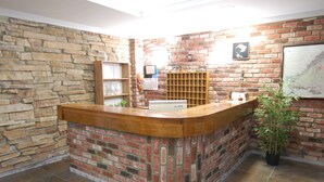 A reception area with a wooden reception desk, a stone wall, a brick wall, a calendar, a map, and a potted plant. - Hostal El 36 (Sesena)