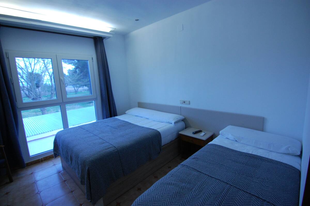 A hotel room with two beds, a window with curtains, and a wooden floor.