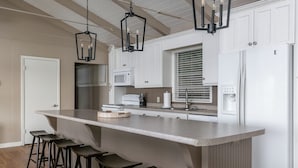 Eine moderne Küche mit Kochinsel, Barhocker, weißen Schränken und einem eingebauten Mikrowellenherd.