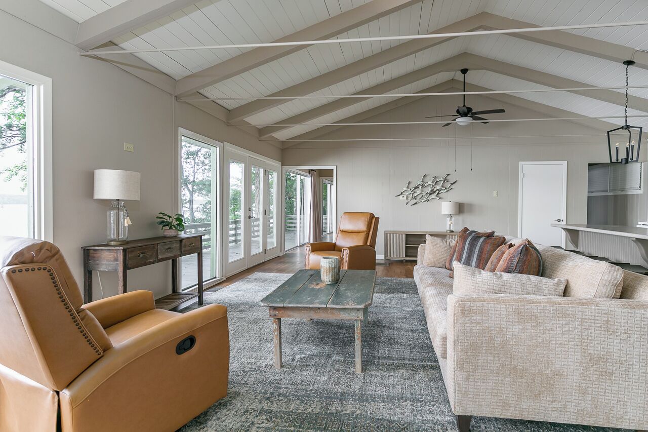 A spacious living room with a high ceiling, a large window, a sofa, a chair, and a coffee table.