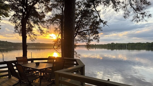 Eine Holzterrasse mit Sitzgelegenheiten und Blick auf einen See bei Sonnenuntergang.