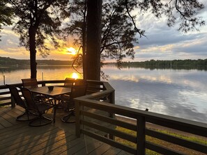 A wooden deck with outdoor seating and a view of a lake at sunset.