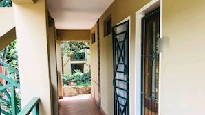 Un pasillo con suelo de baldosas, barandilla verde y una puerta con reja de metal.