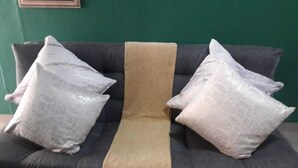 Un sofá gris con una manta beige y dos almohadas grises.