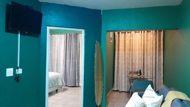 Una habitación con paredes color turquesa, una cama con colcha blanca, una mesita con superficie de vidrio y una silla.