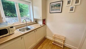 A kitchen with a microwave, sink, and wooden floor. - Morfach Charming Modern Cottage within Conwy walls (Morfach)