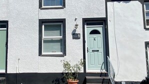 A two-story building with a white exterior, a green door, and a small potted plant on the ground floor. - Morfach Charming Modern Cottage within Conwy walls (Morfach)