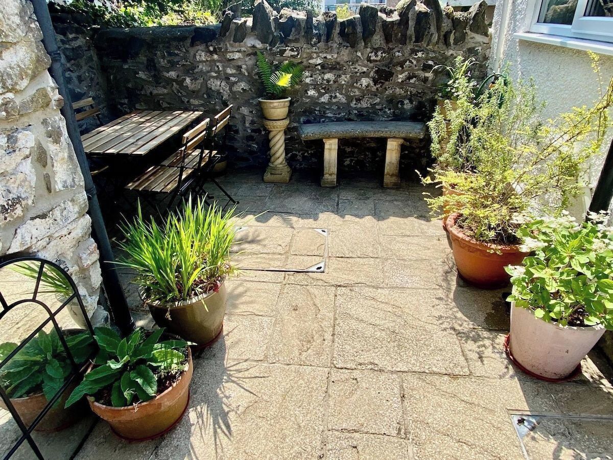 Un patio in pietra con tavolo e panche in legno, circondato da piante in vaso.