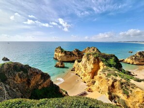 A coastal landscape with rocky formations, clear blue water, and a sandy beach.
