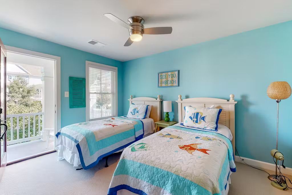Un dormitorio con dos camas, un ventilador de techo, una ventana con contraventanas y una decoración de pared con temática playera.