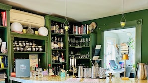 A bar area with green walls, a white counter, and two blue bar stools. There are shelves with bottles and glasses, and a sign that reads "NOTICE".