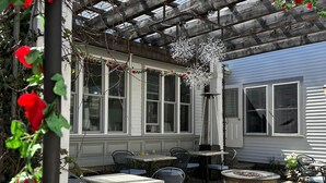 A covered patio area with tables and chairs, a fire pit, and a pergola with climbing roses.