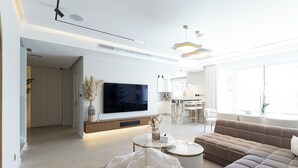 Een moderne woonkamer met een flatscreen televisie, een bank, een salontafel en een eethoek op de achtergrond.