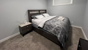 A bedroom with a bed, nightstand, and a wall-mounted light fixture. - Modern, well furnished 1 bedroom home with free street parking (Spruce Grove)