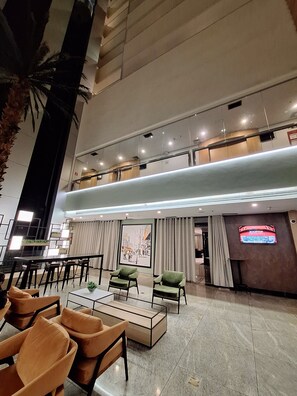 Een ruime lobby met een hoge plafond, een bar en zithoeken.