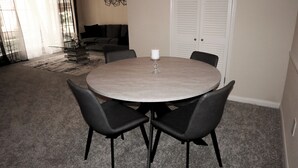 Uma mesa de jantar redonda com quatro cadeiras pretas, uma vela branca e um castiçal de vidro.