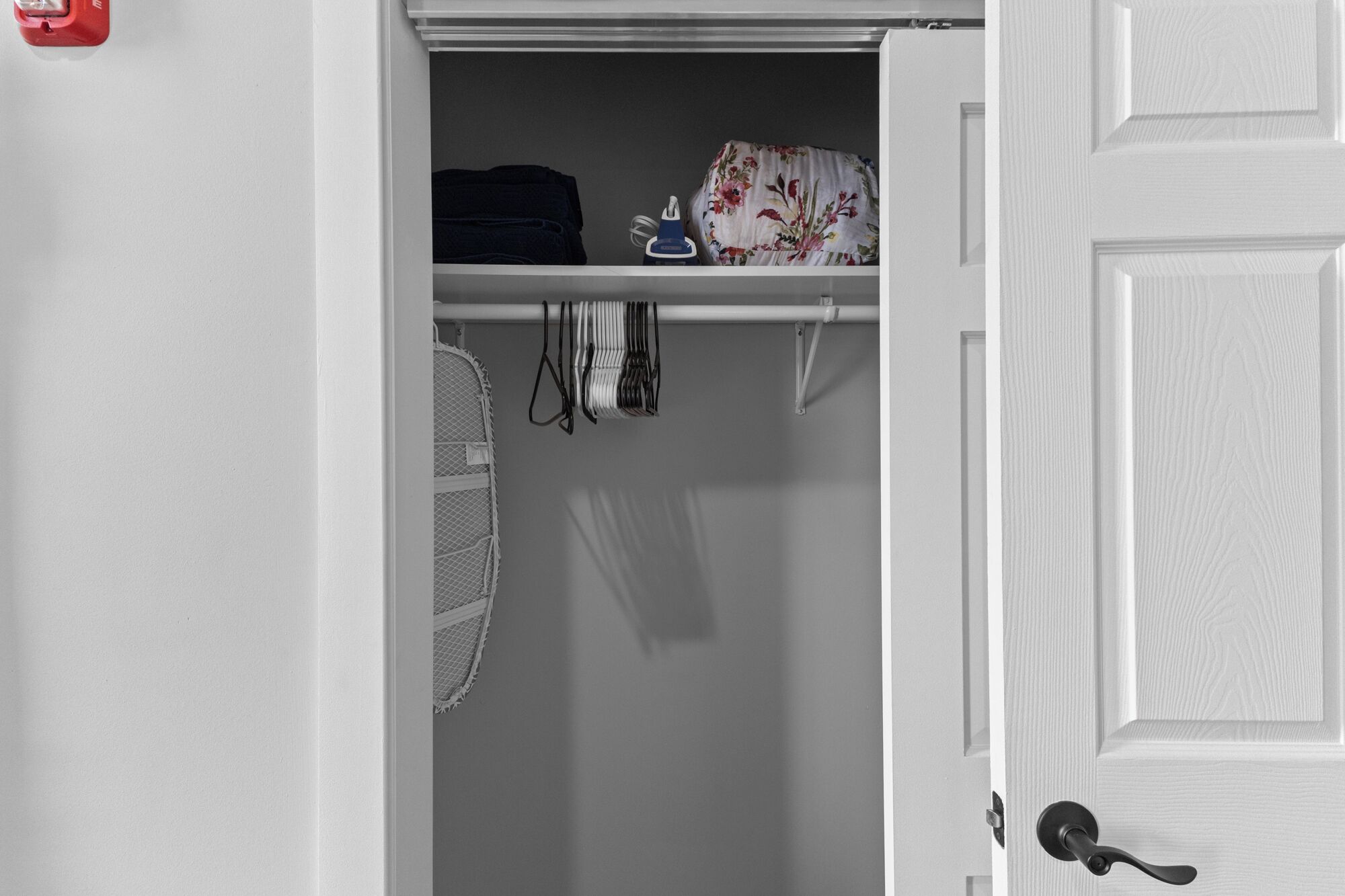 A closet with folded clothes, a fan, and a floral-patterned item on a shelf.