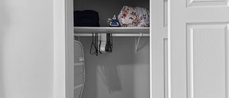 A closet with folded clothes, a fan, and a floral-patterned item on a shelf.