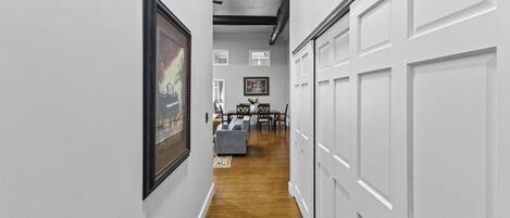A hallway with white walls, wooden flooring, and a dining area with a table and chairs.