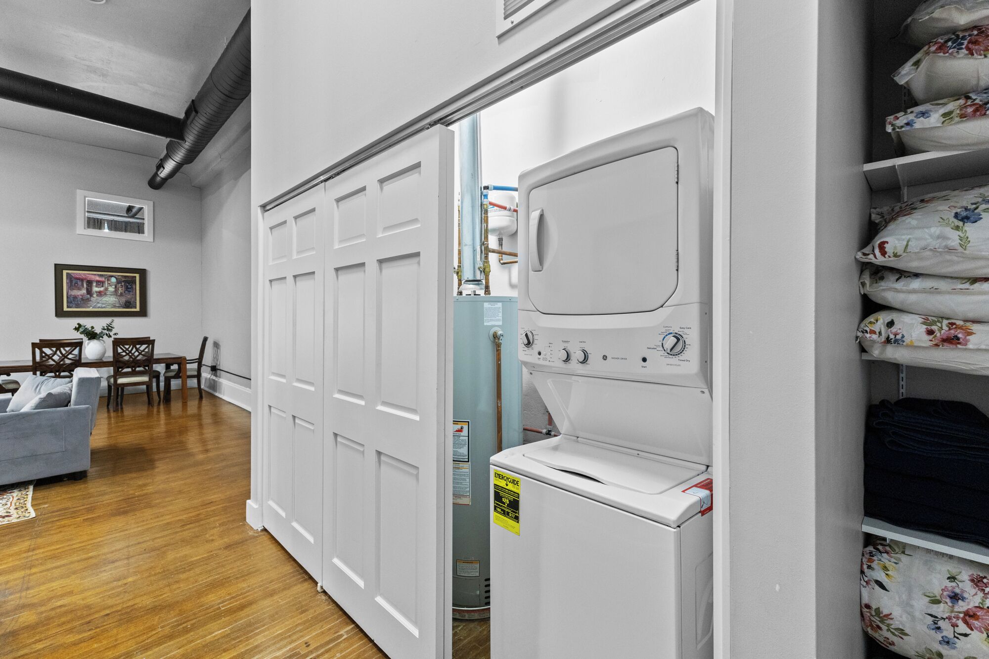 A laundry room with a stacked washer and dryer, a dining area with a table and chairs, and a hallway with a door leading to another room.