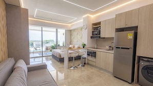 A modern kitchen with a built-in oven, a stainless steel refrigerator, and a dishwasher. There is a dining area with a table and chairs, and a large window offering a view of the outdoors.