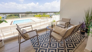 A balcony with a pool, two chairs, a patterned rug, and potted plants.