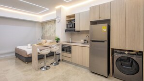 A modern kitchen with a built-in washing machine, a dining area with a bar stool, and a small seating area with a sofa and a table.