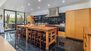 A modern kitchen with a wooden island, bar stools, and a stainless steel range hood. - Modern, Ultra-Luxurious, 5 BR/4.5 BA Home on a quiet wooded lake in Ann Arbor (Superior Township)