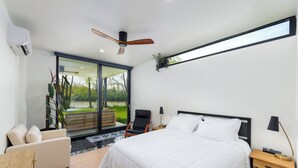 A modern bedroom with a large bed, a chair, a nightstand, and a ceiling fan. - Modern, Ultra-Luxurious, 5 BR/4.5 BA Home on a quiet wooded lake in Ann Arbor (Superior Township)