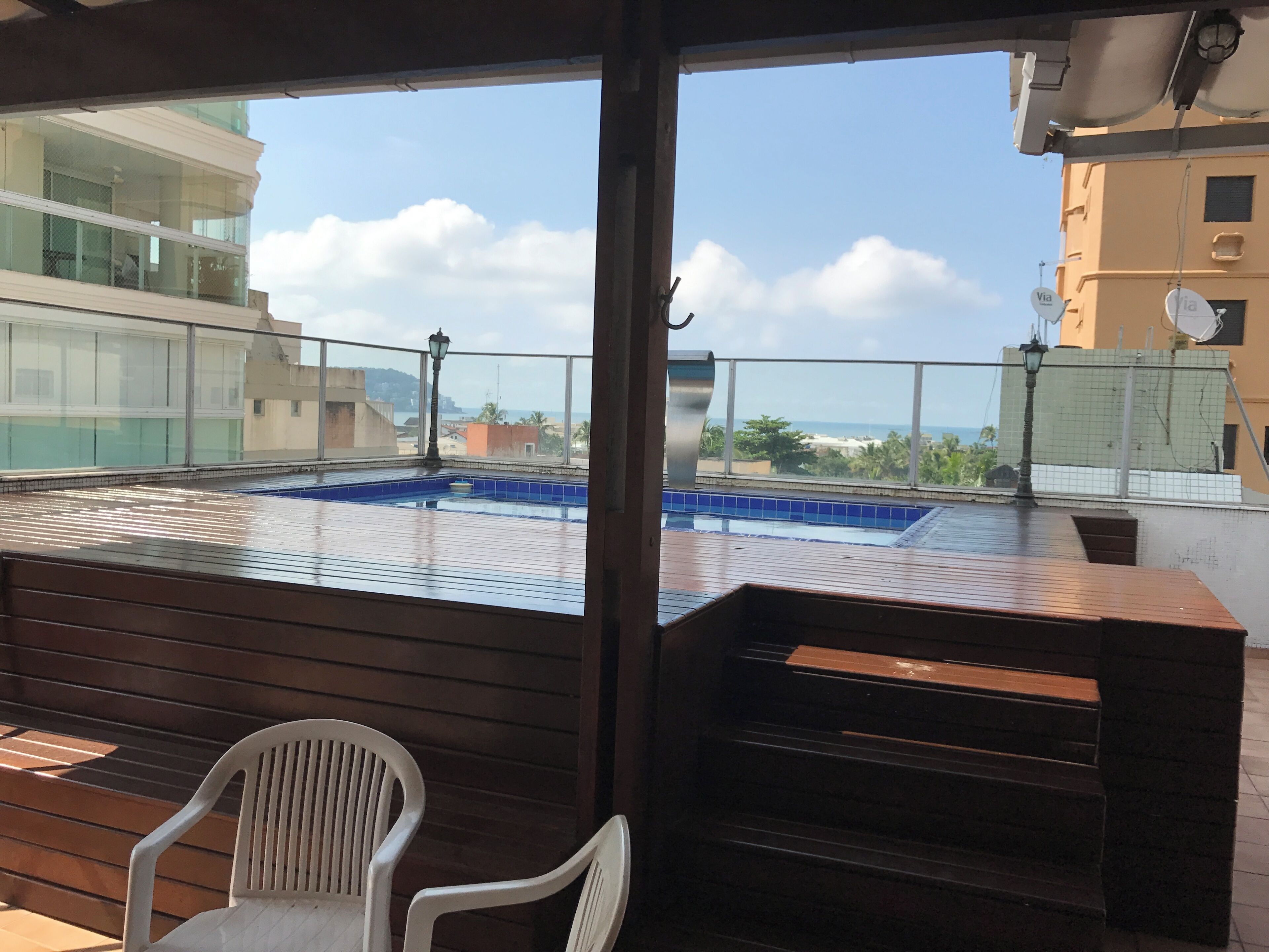 A rooftop pool with a view of the cityscape, a wooden deck, and a white plastic chair.