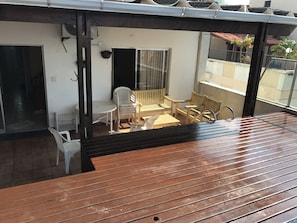 A balcony with wooden flooring, a white plastic chair, a wooden bench, and a table. - PENTHOUSE PENTHOUSE (Balneario Cidade Atlantica Guarujá)