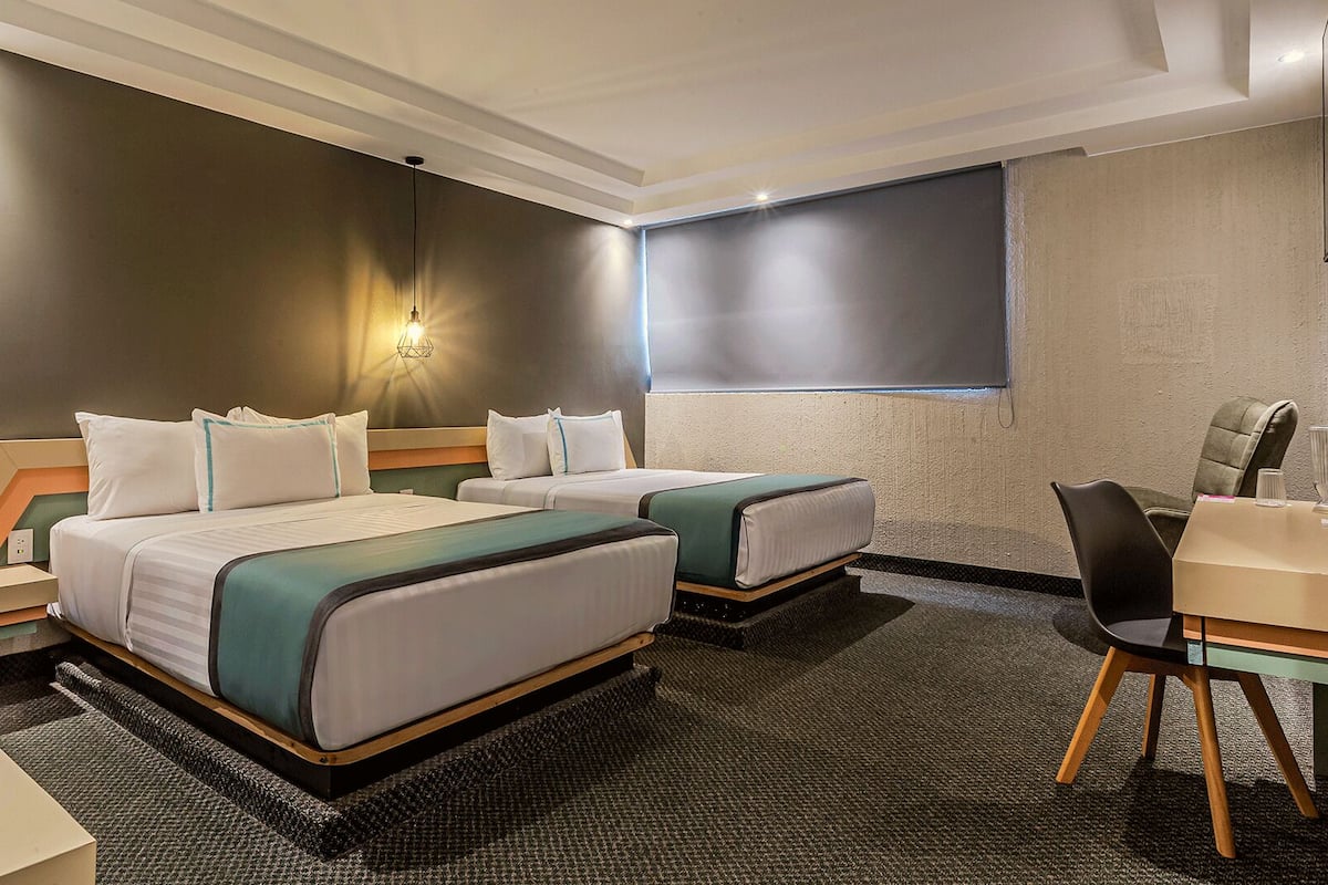 A hotel room with two beds, a desk, a chair, and a window.