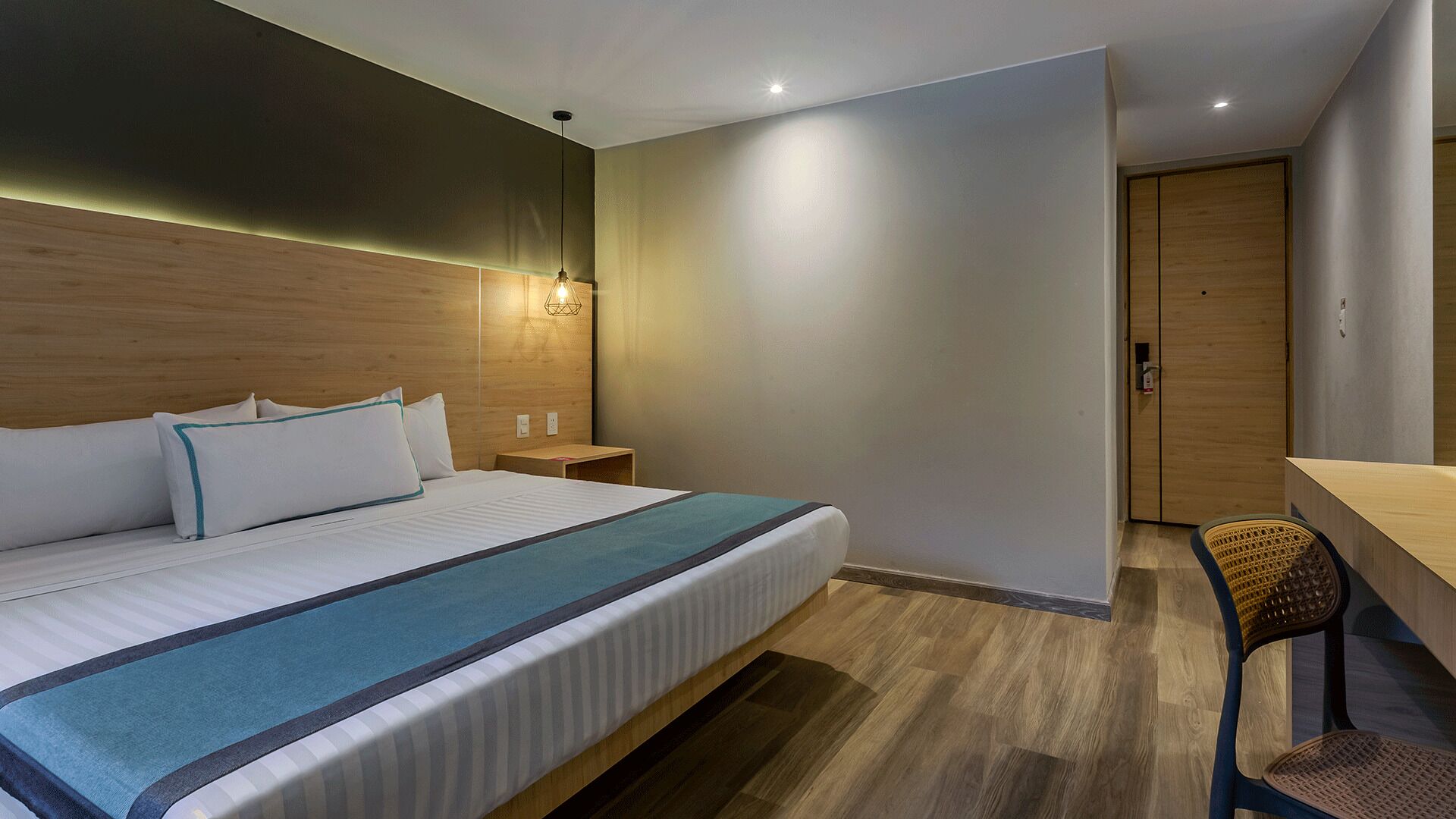 Une chambre d’hôtel avec un lit, une table de chevet, une lampe, une chaise et une porte.