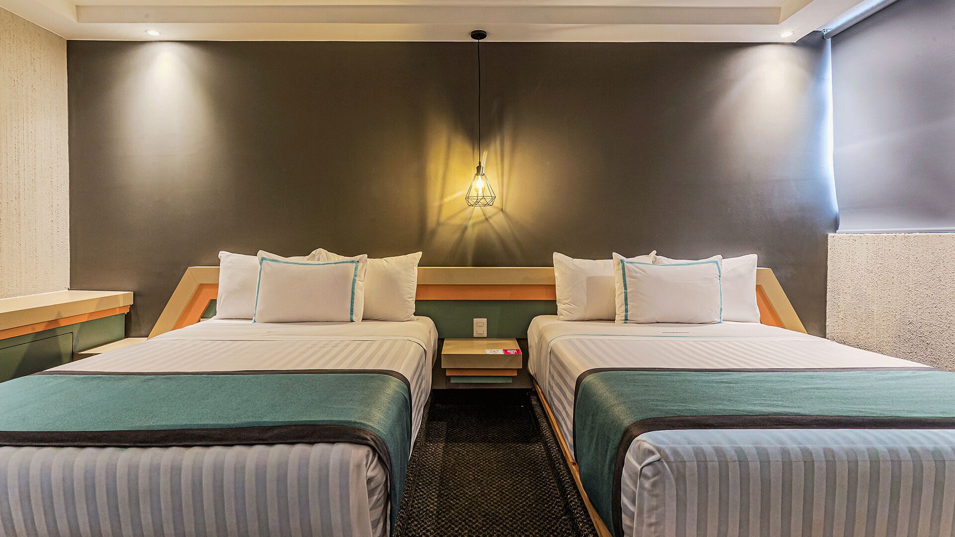 A hotel room with two beds, a nightstand, a wall-mounted light, and a window.