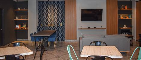 A modern lounge area with a dining table, blue chairs, a grey sofa, and a flat-screen TV mounted on the wall.