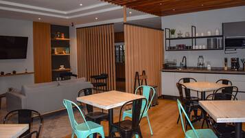 Un comedor moderno con mesas y sillas de madera, una cocina con electrodomésticos y un televisor montado en la pared.