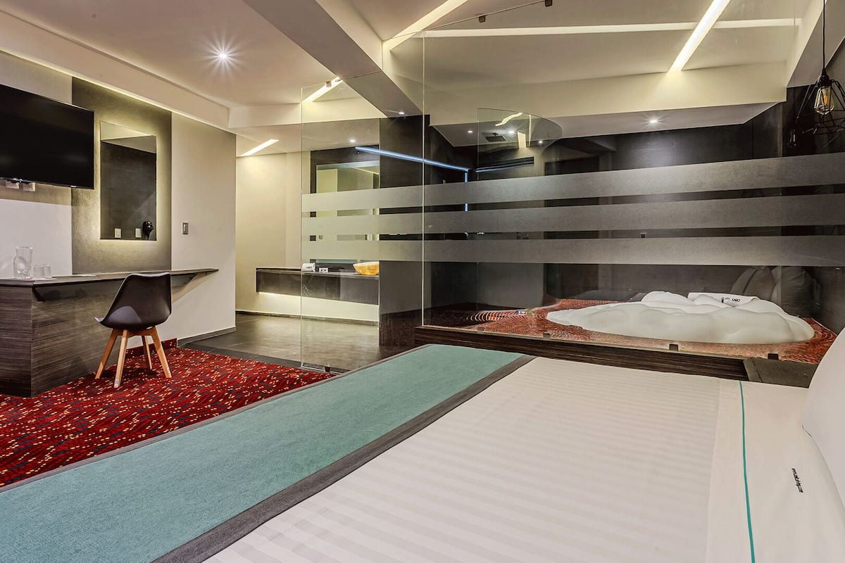 A modern hotel room with a bed, a desk, a TV, and a bathroom with a glass partition.