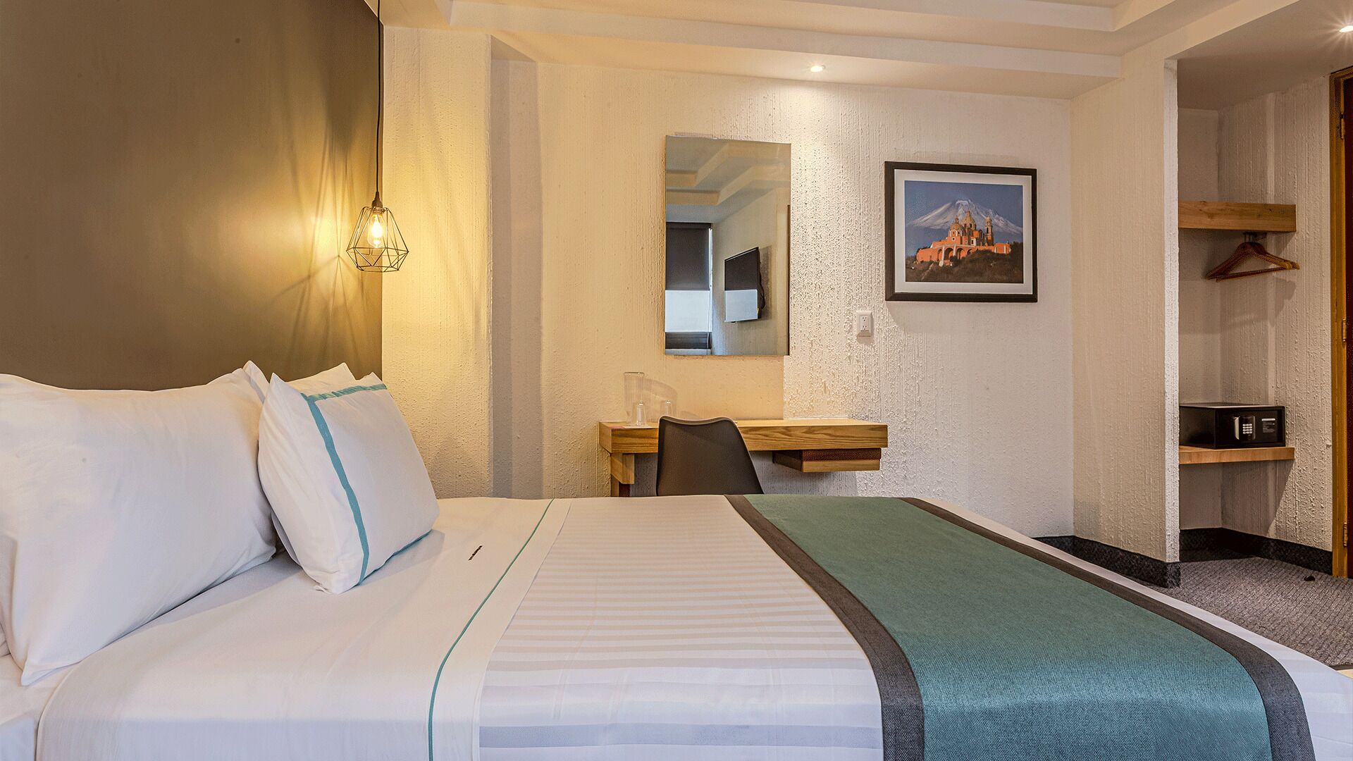 Ein Hotelzimmer mit Bett, Schreibtisch, Stuhl, Spiegel, einem Bild an der Wand und einer Mikrowelle.