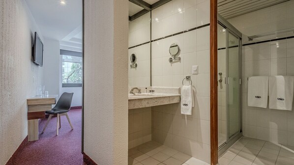 A modern bathroom with a shower, a sink with a mirror, and a chair. - Uniko Living Roma (Mexico City)