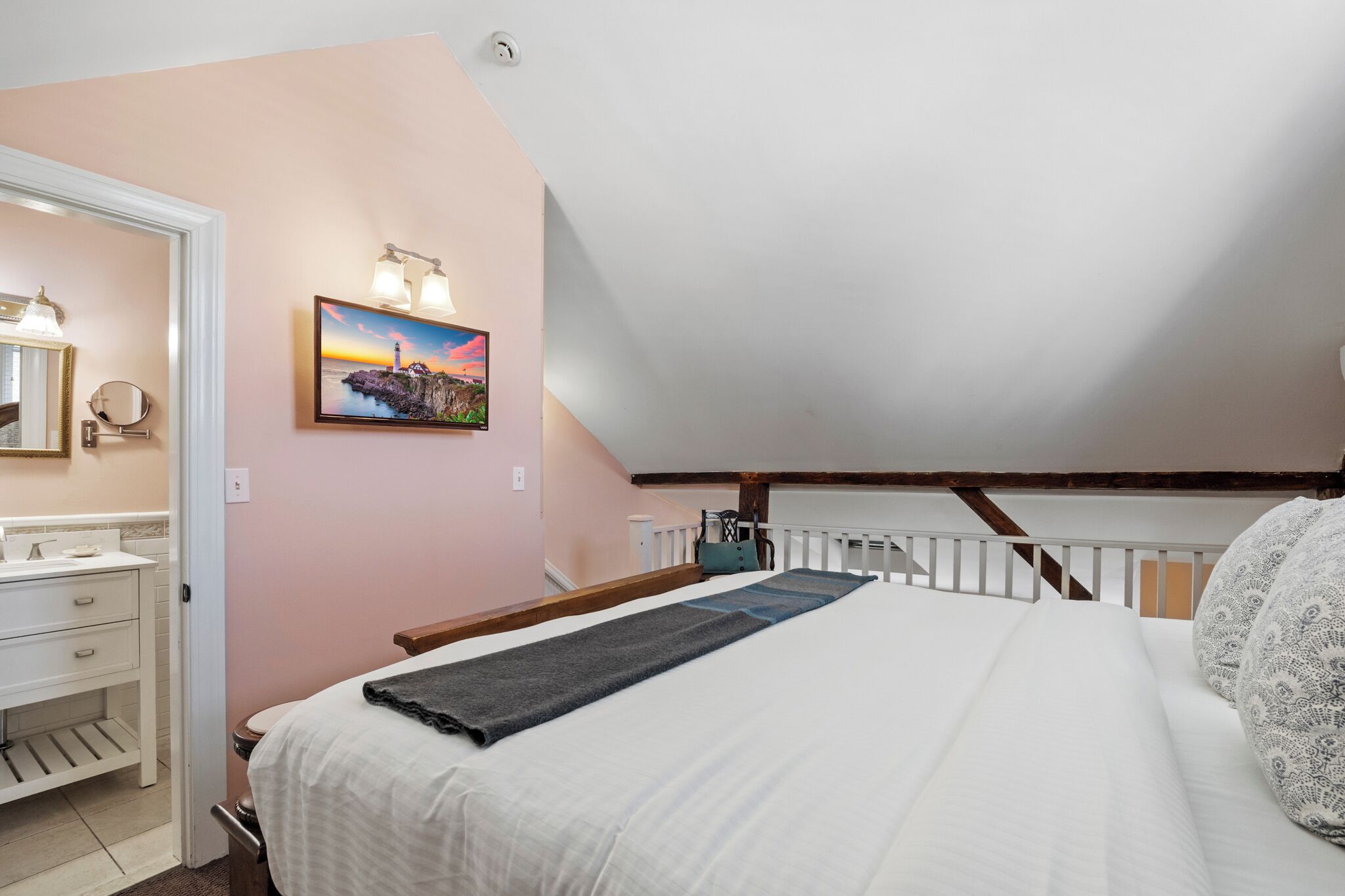 A bedroom with a bed, a nightstand, a dresser, a painting, and a sloped ceiling.